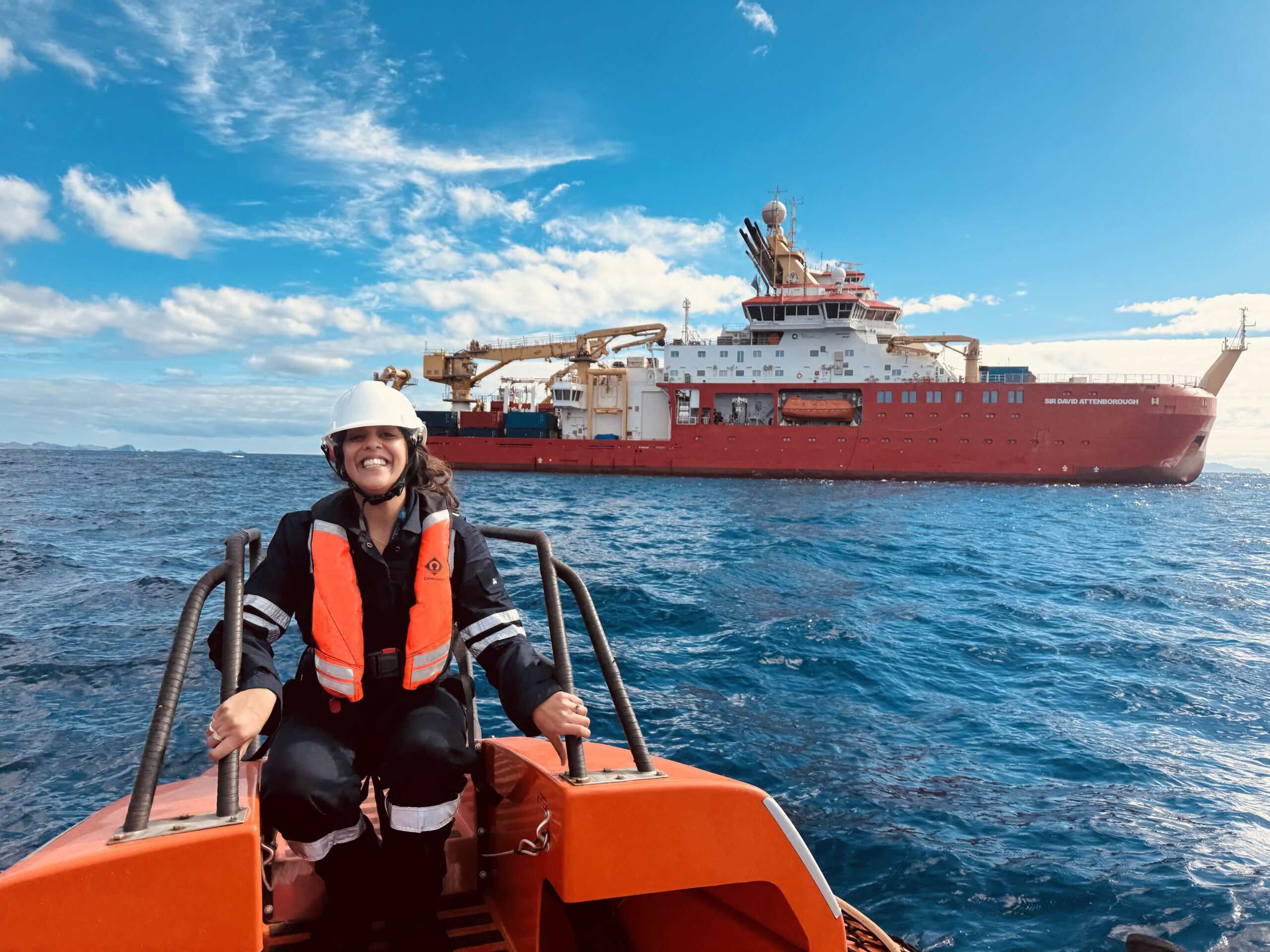 A smiling female on a small boat with the RRS Sir David Attenborough in the background