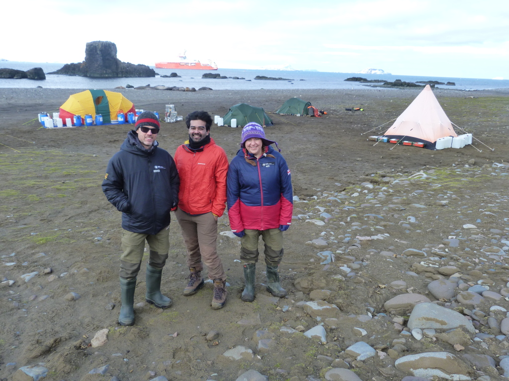 A group of people standing on top of a rocky beach with tents behind them