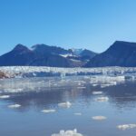 A body of water with a mountain in the background, ice floats on the water surface.