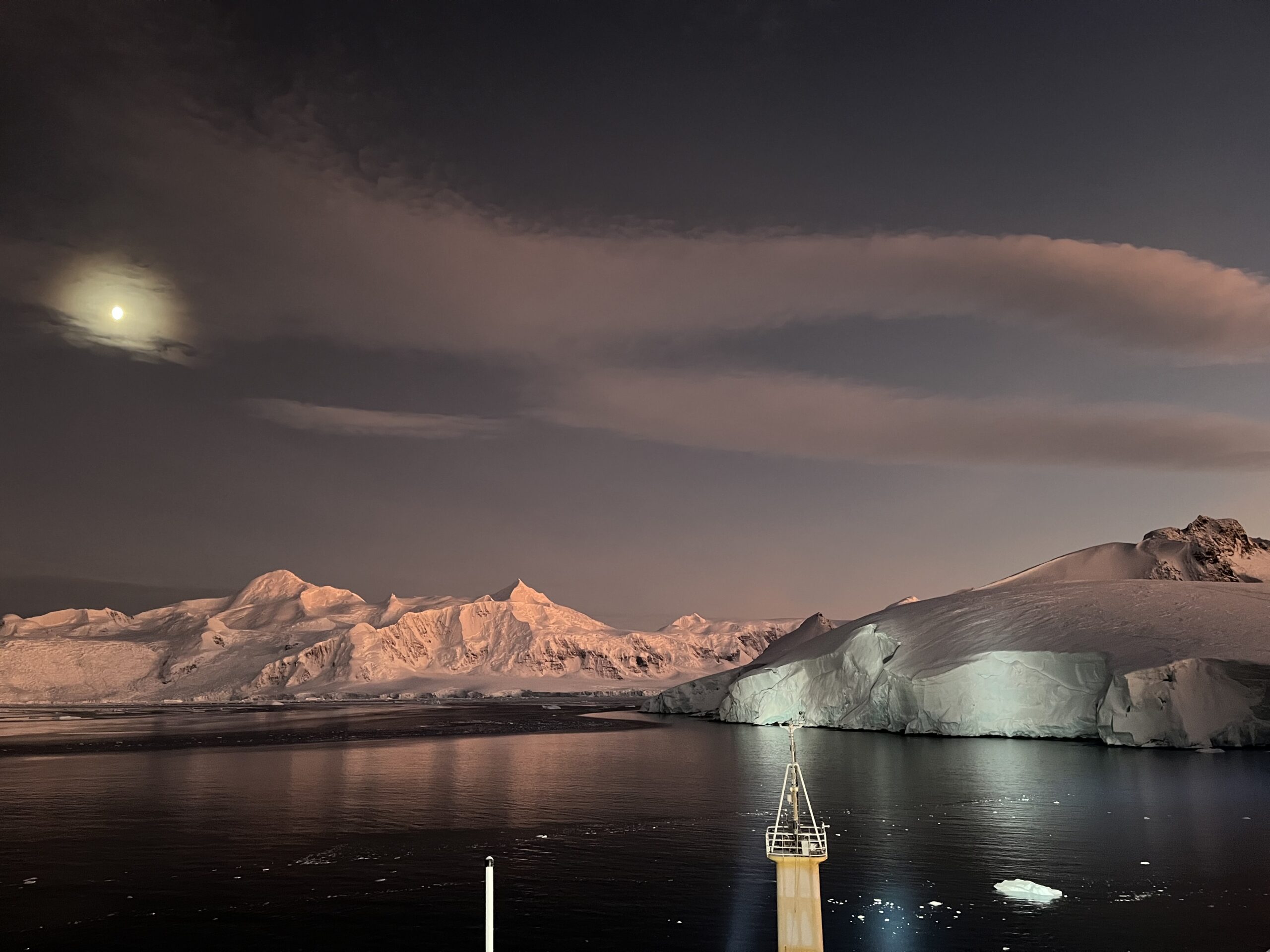 A large body of water with a snowy capped mountain in the background, and icy glacier in the foreground. 