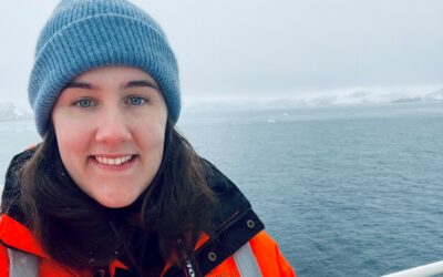A person wearing a jacket and hat in front of a body of water