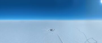 An arial photo of research camp, Little Dome C, on Antarctic ice far in the distance beneath a bright blue sky.