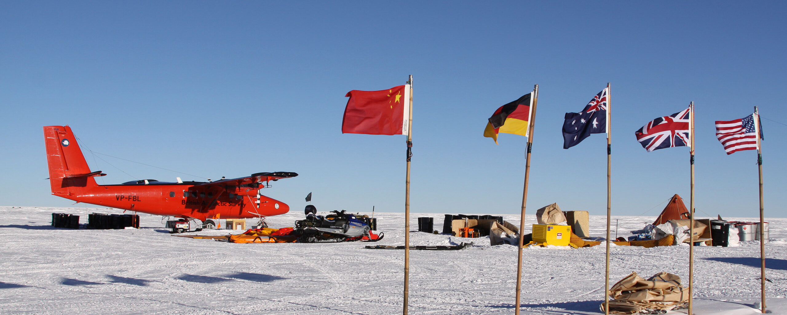 A twin otter at a field camp with flags of China, Germany, Australia, the UK and United States in the foreground