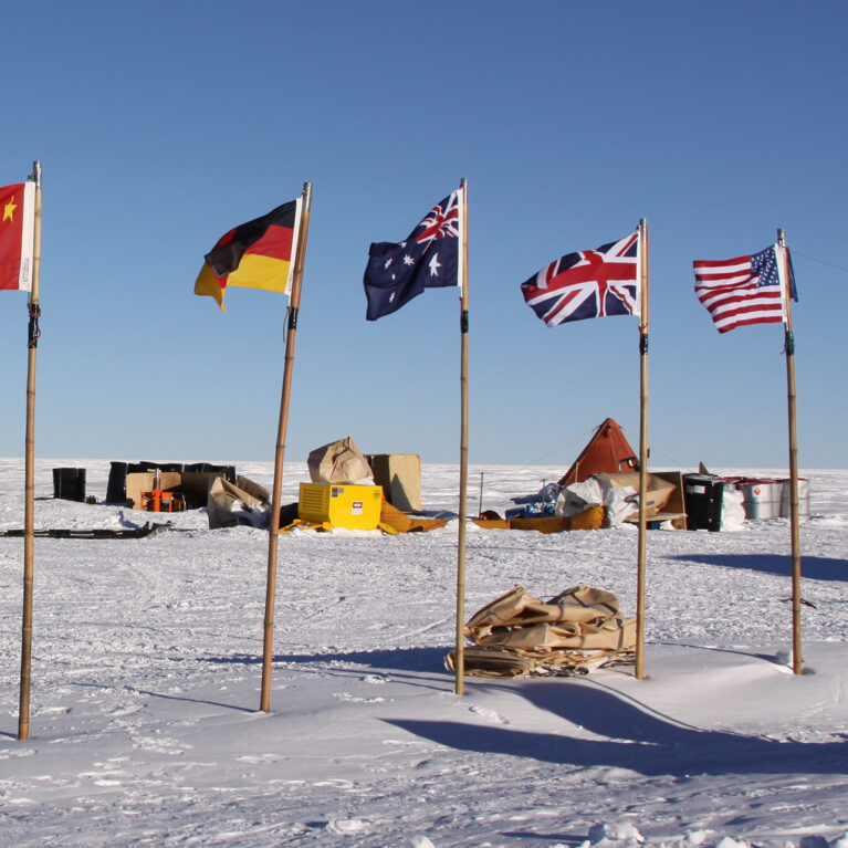A twin otter at a field camp with flags of China, Germany, Australia, the UK and United States in the foreground