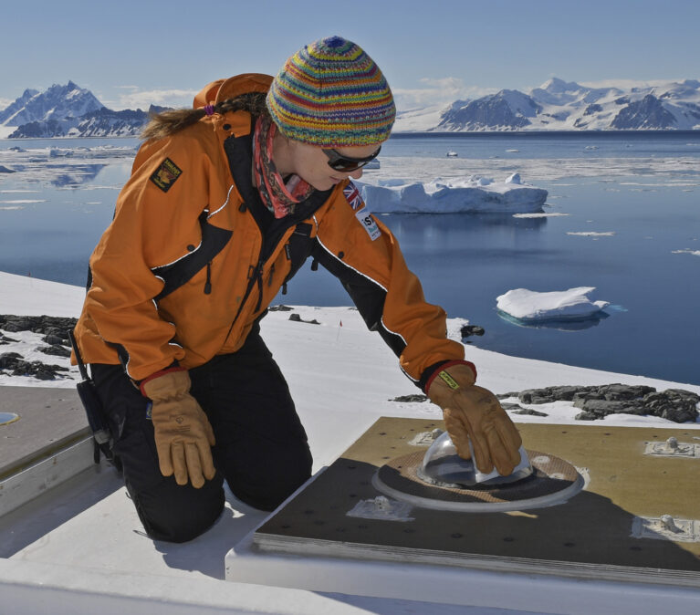 A scientist maintaining an optical instrument on an ice shelf.