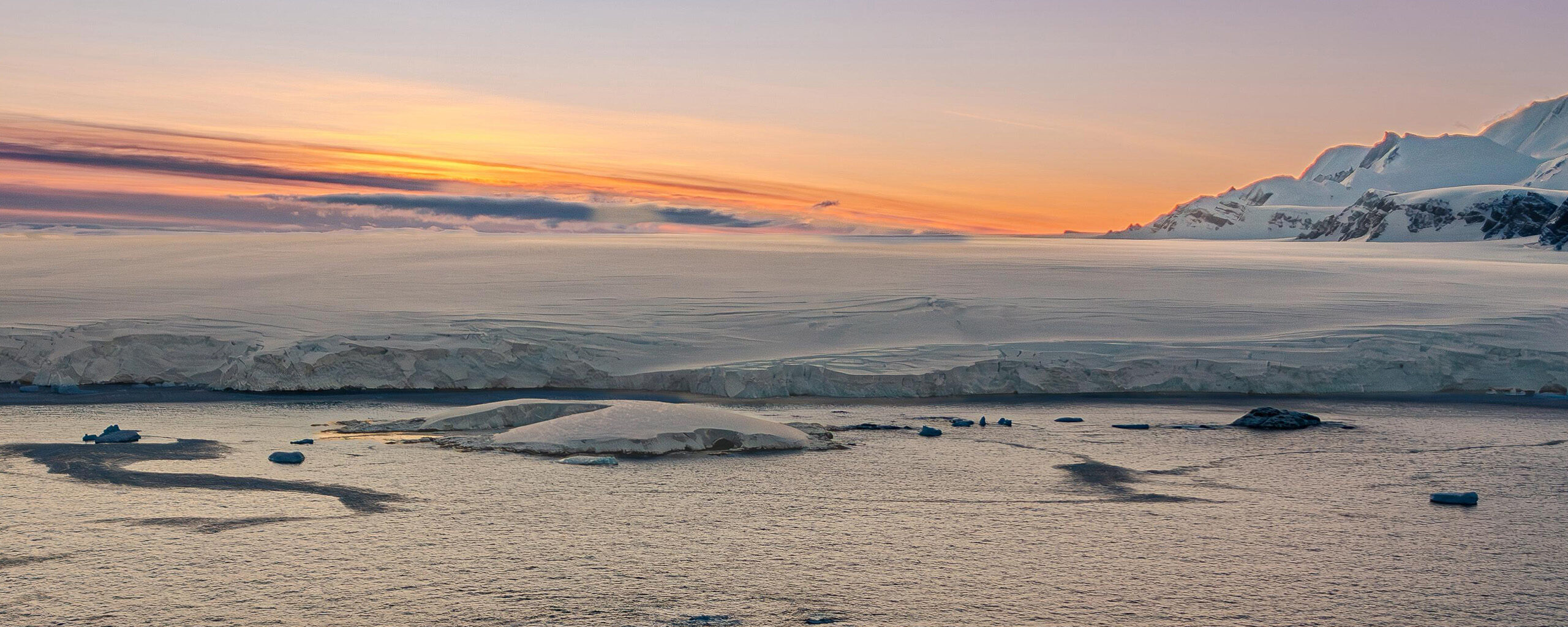 An Antarctic sunset. The ice shelf meets the sea with mountains in the background