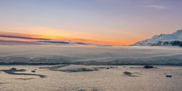 An Antarctic sunset. The ice shelf meets the sea with mountains in the background
