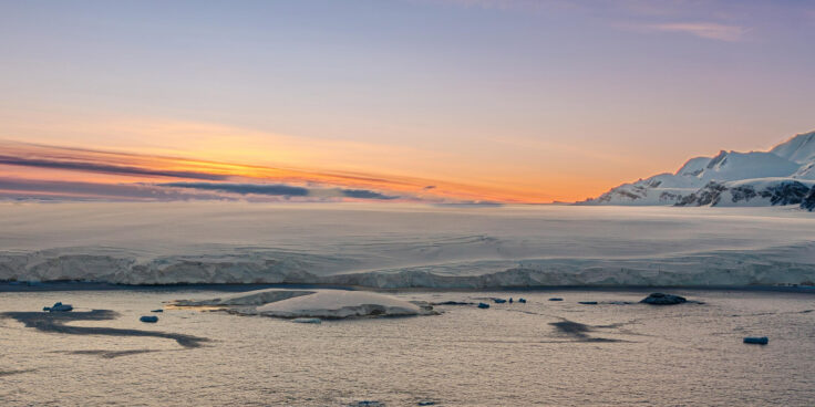 An Antarctic sunset. The ice shelf meets the sea with mountains in the background