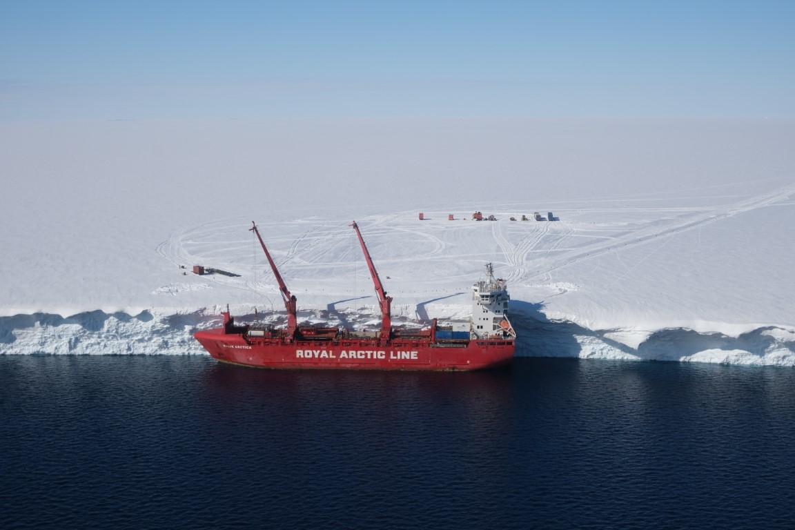 A boat in a large body of water alongside a shelf of snow and ice