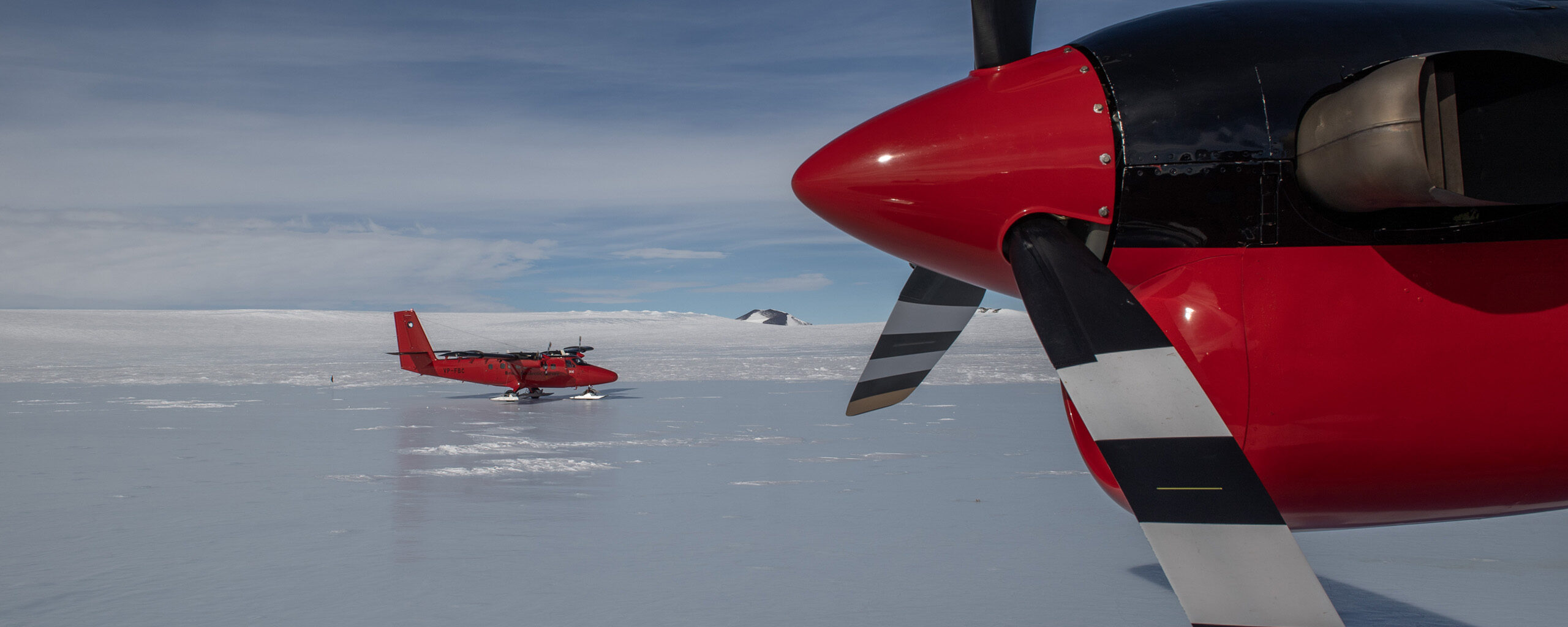Two twin otter propeller planes that have landed on blue ice.