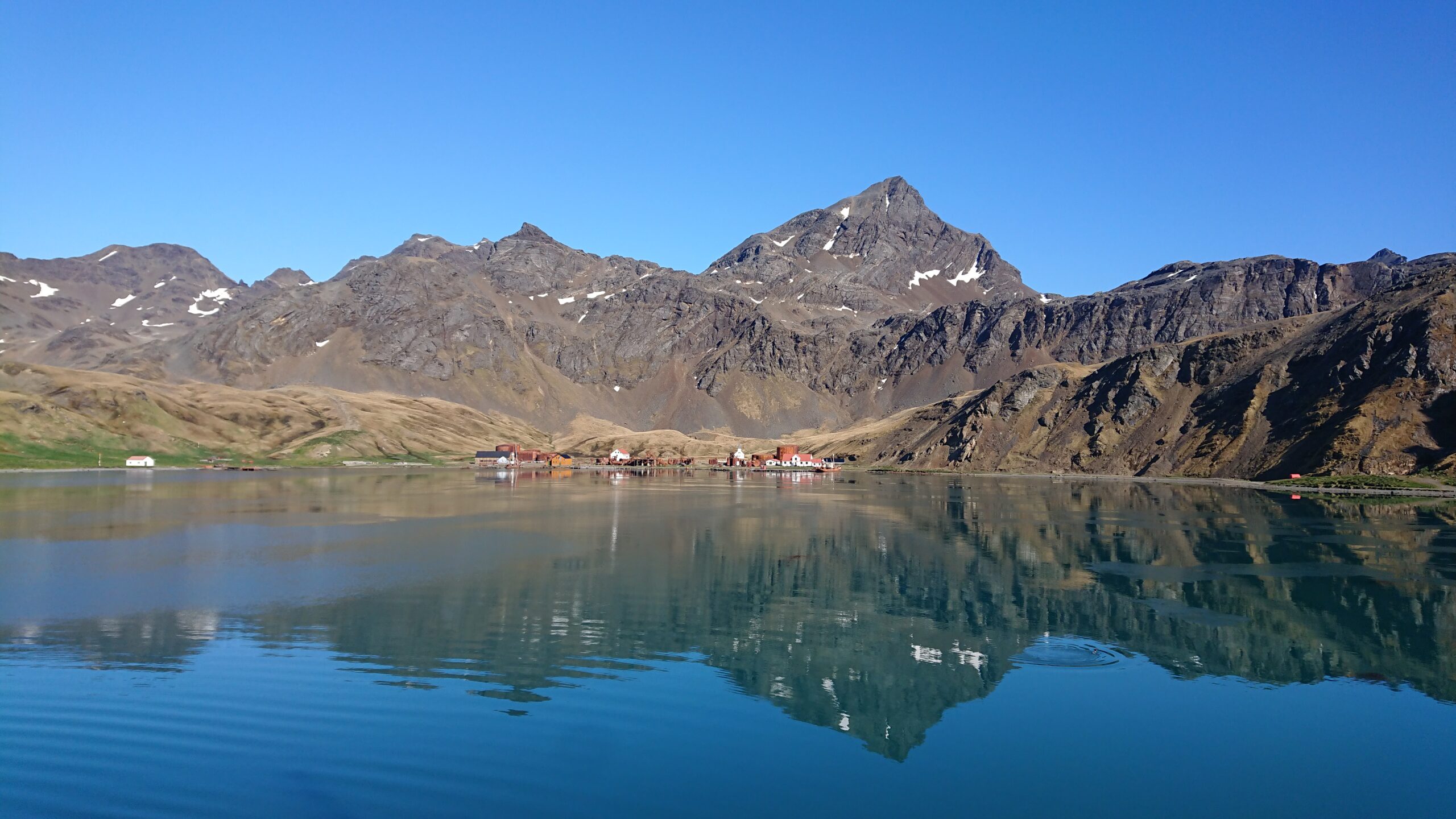 A mountain landscape behind a large body of water with the landscape reflected in the water.