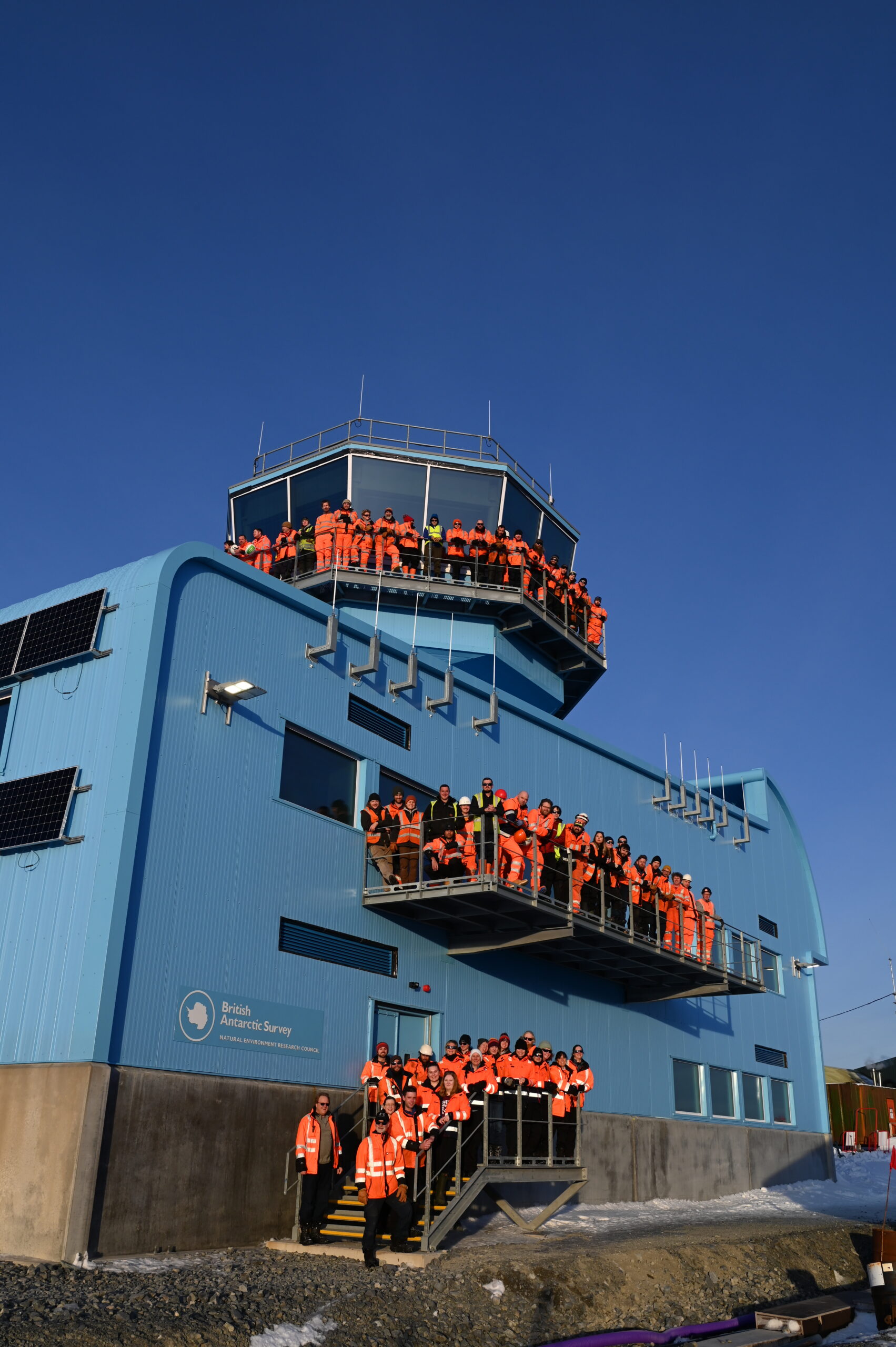  A team of people standing on the stairwell outside a large blue building. 