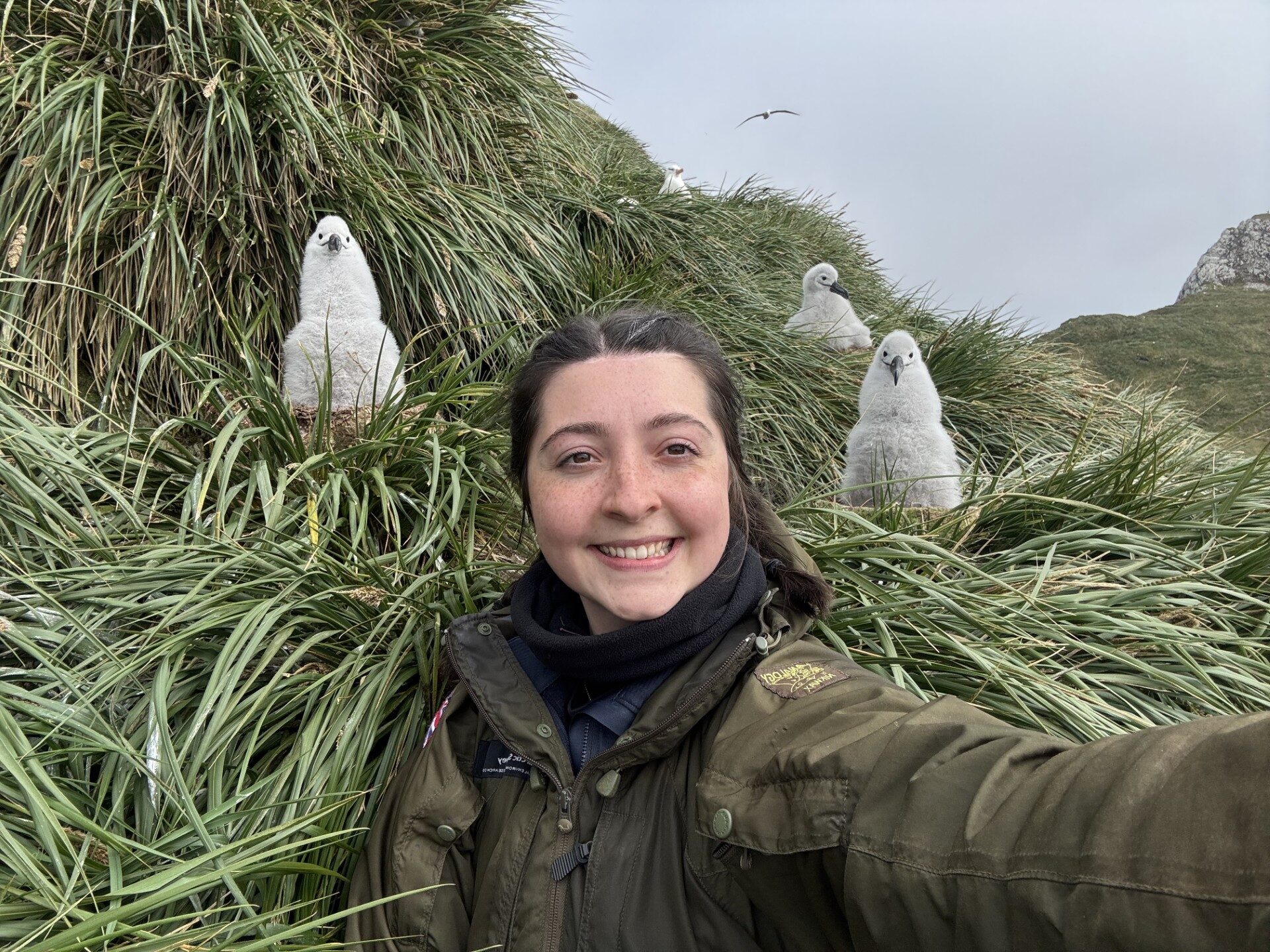 A person posing for the camera with some large fluff white birds behind them