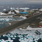 aerial view of an antarctic research station with a runway and a large blue building