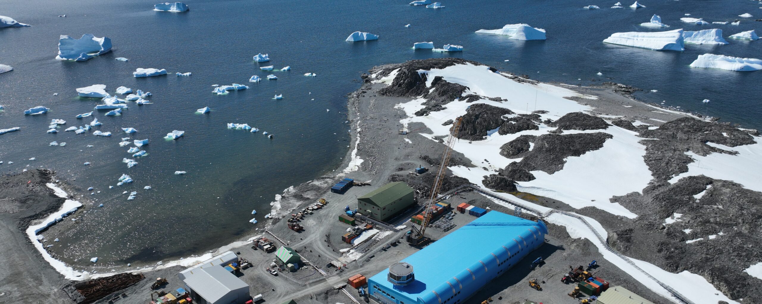 A large blue building surrounded by water and snowy mountains in the background.
