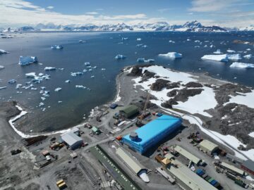 A large blue building surrounded by water and snowy mountains in the background.