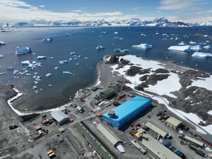 A large blue building surrounded by water and snowy mountains in the background.