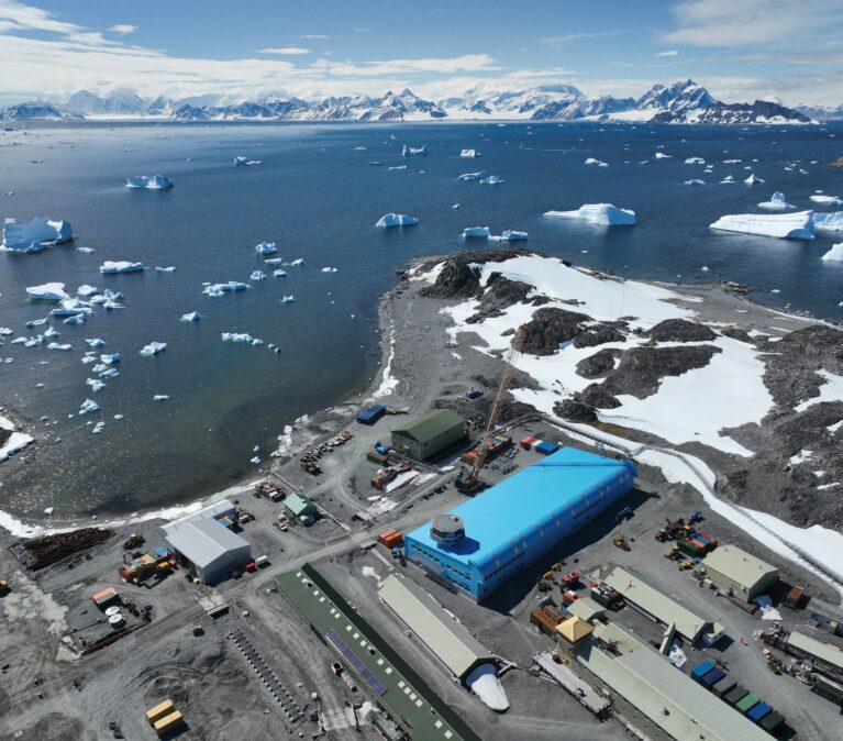 A large blue building surrounded by water and snowy mountains in the background.