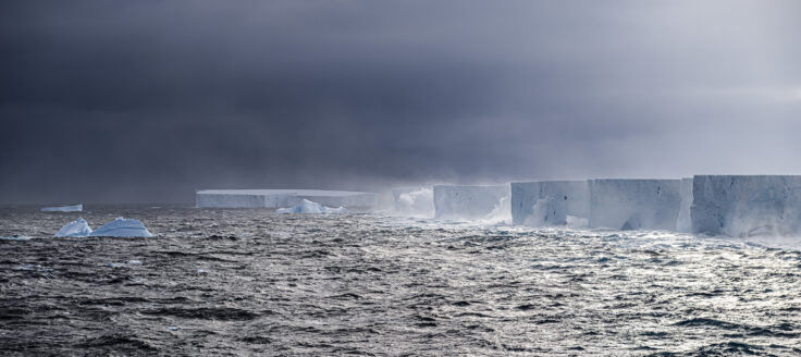 Edge of A23a giant iceberg floating in the ocean with waves crashing against it.