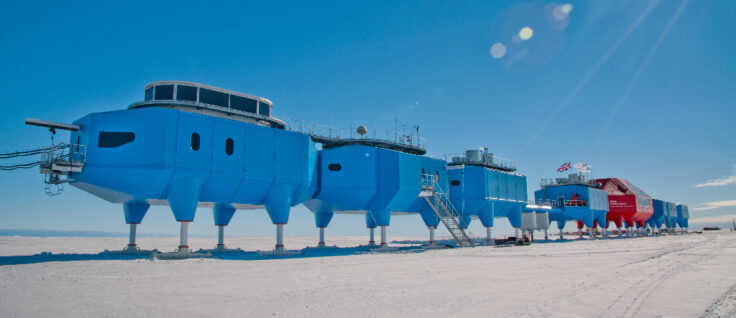 Blue building modules on stilts over the Brunt ice shelf in Antarctica against a bright blue sky.