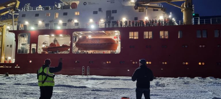 A person standing in front of a large ship in the water