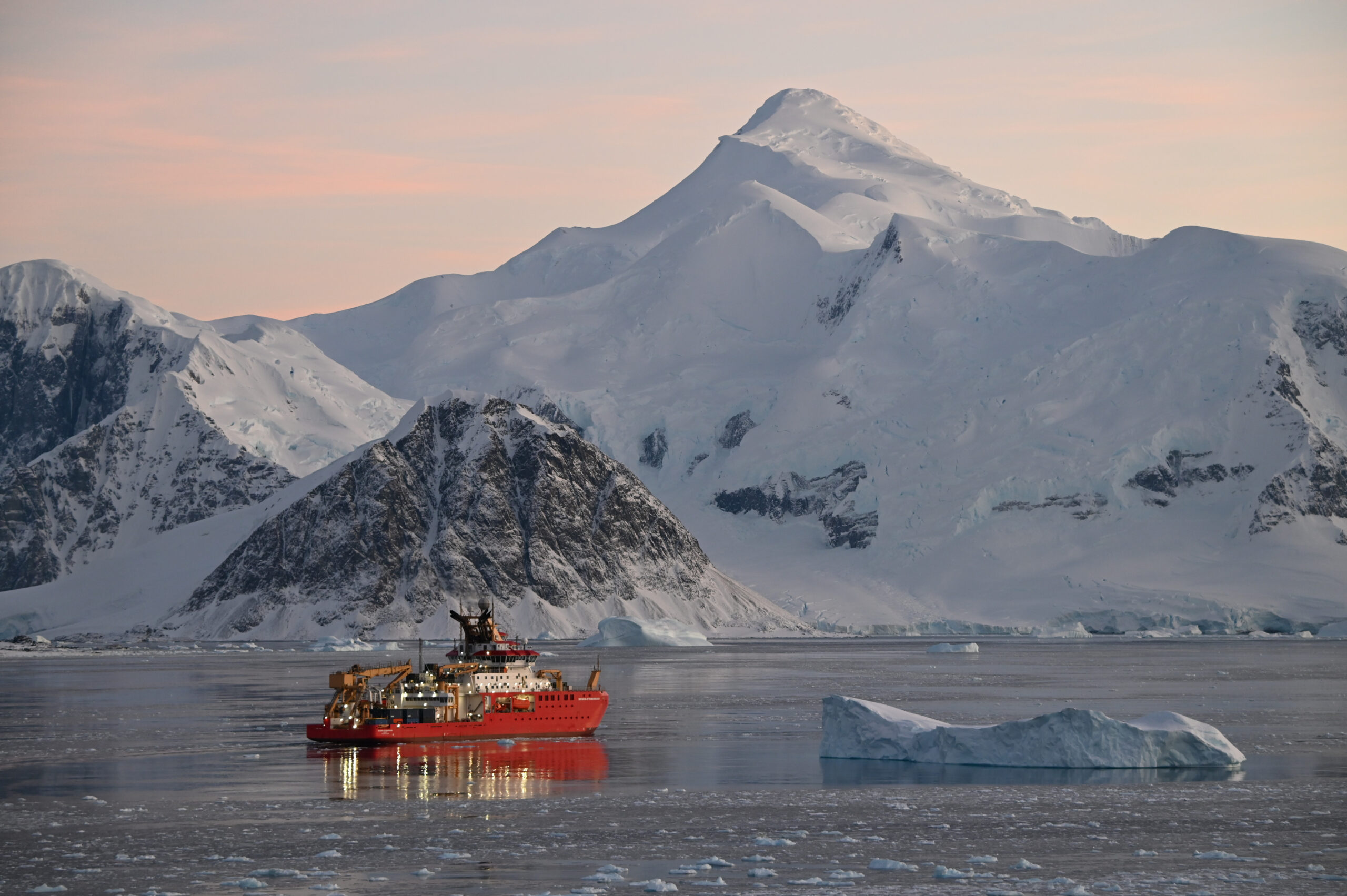 The research ship, Sir David Attenborough sails past a snowy mountain.