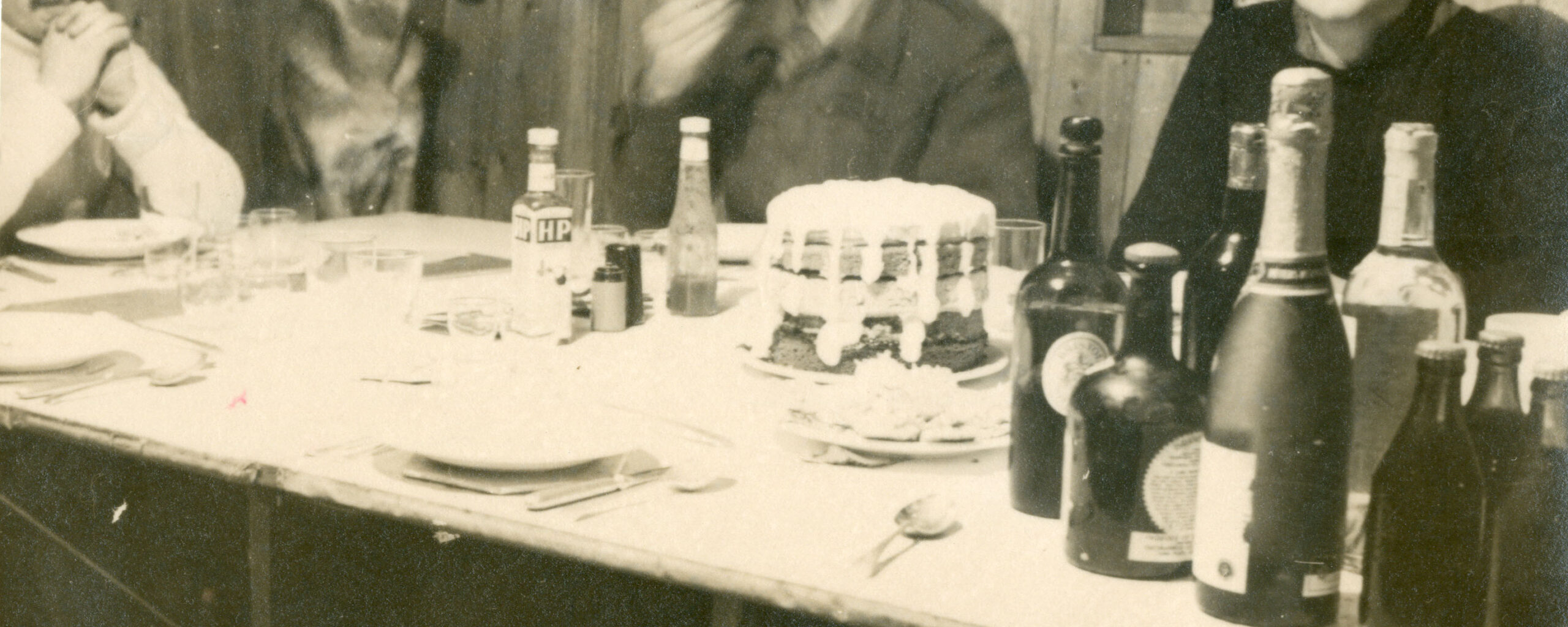 Three men and a dog sit around a table with a cake and drinks bottles.