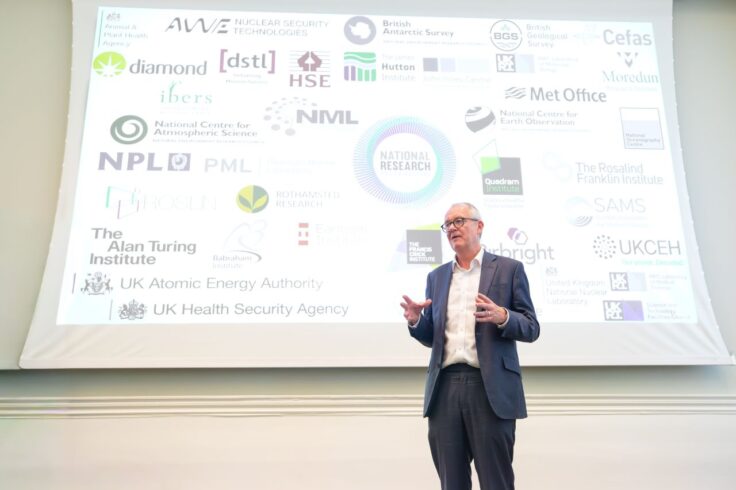 Man in a business suit speaking in front of a board of logos.