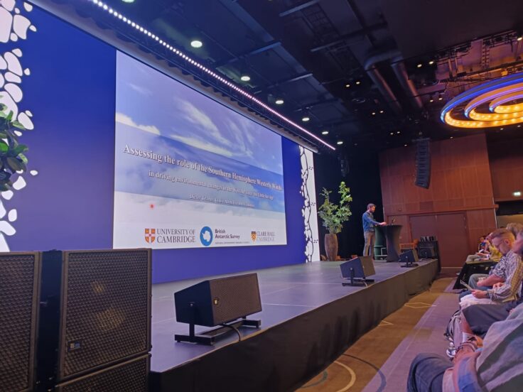 A man presents research on a stage with a big screen.