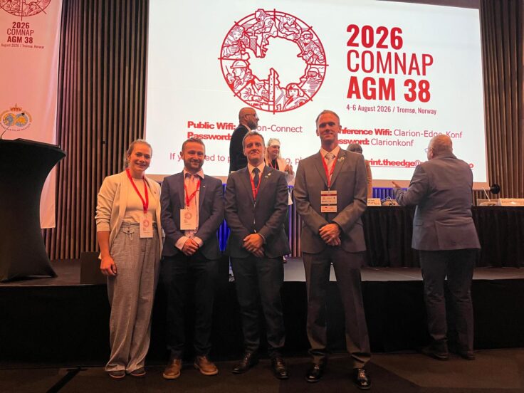 A group of people standing in front of a presentation screen in a conference room posing for the camera.