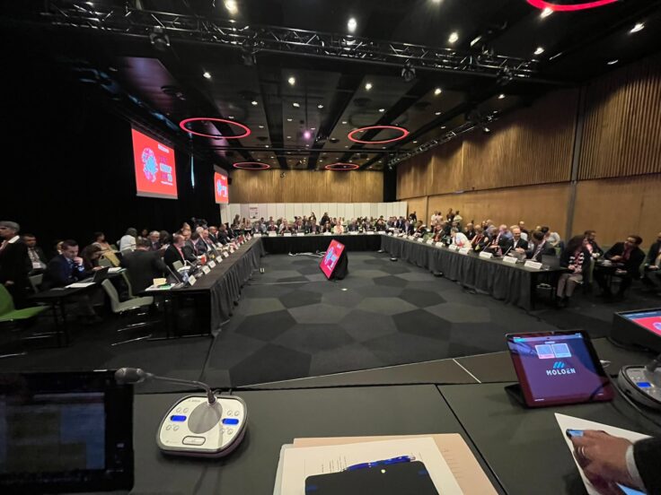 A group of people sitting at a large U-shaped table in a big conference room.