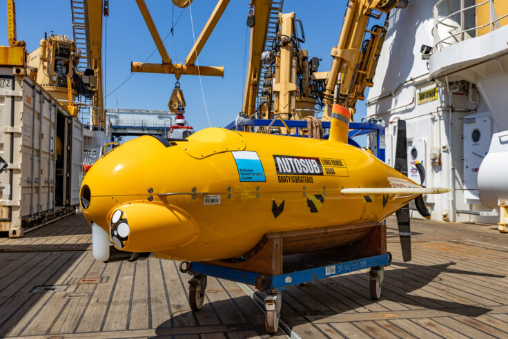 A yellow autonomous submarine on the deck of a research ship.