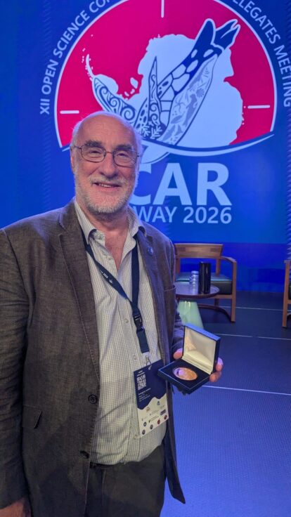 Pete Convey holding up his SCAR medal in front of the SCAR logo and smiling for the camera.