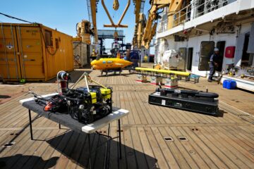 Four underwater robots are laid out on stands on the deck of a research ship.