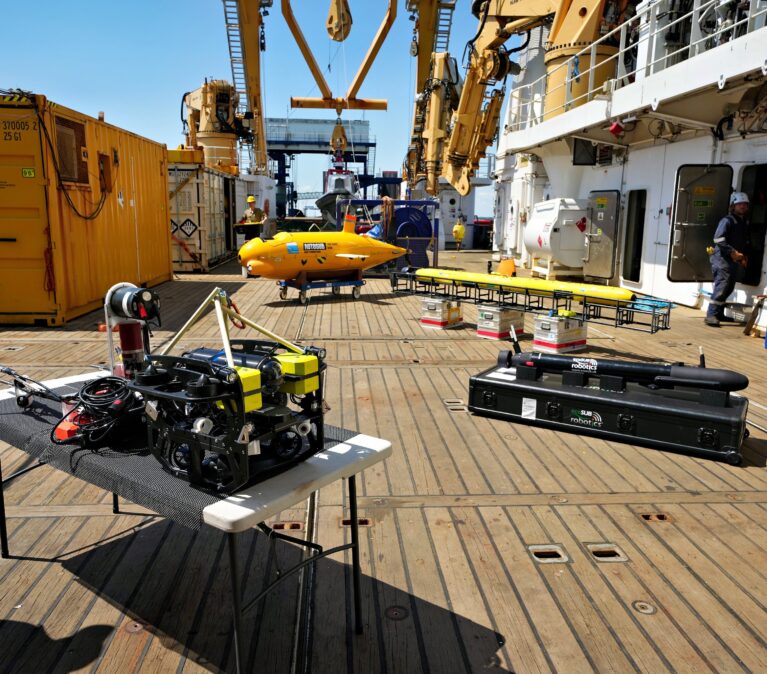 Four underwater robots are laid out on stands on the deck of a research ship.