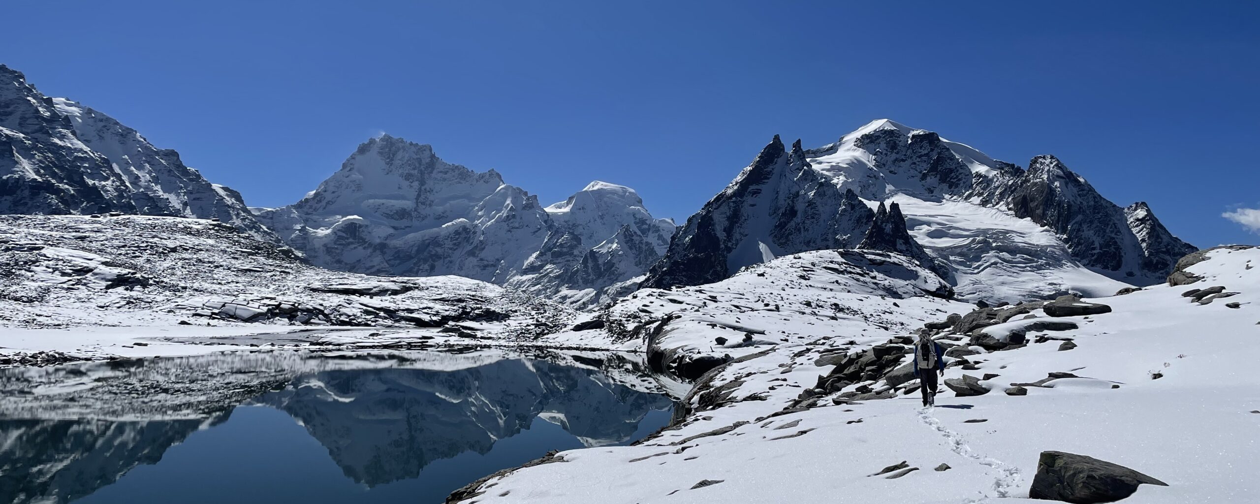 A mountain landscape with a lake and footprints in the snow in the foreground.