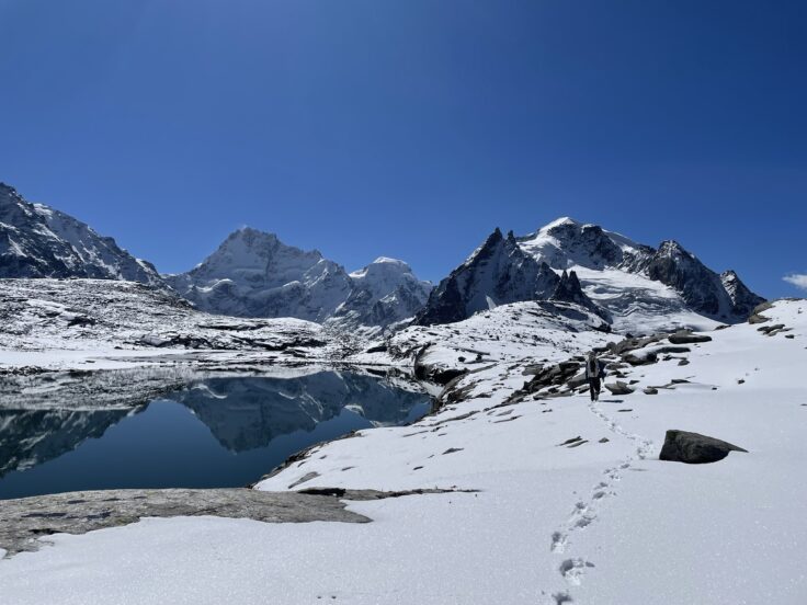 A mountain landscape with a lake and footprints in the snow in the foreground.
