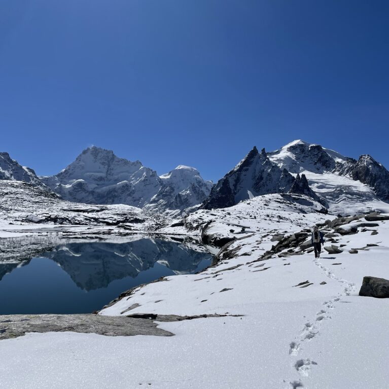 A mountain landscape with a lake and footprints in the snow in the foreground.