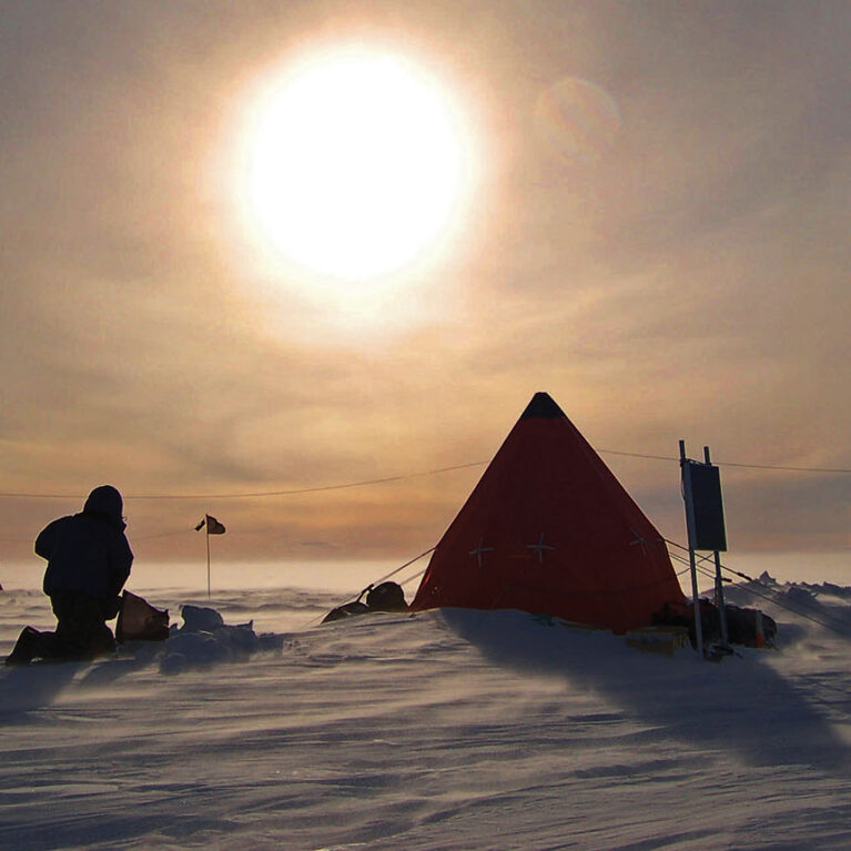 A person and tent in the snow, with a bright sun in the sky
