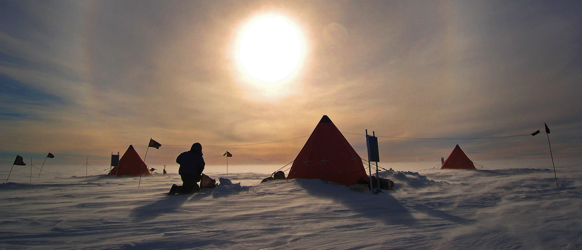 A person and tent in the snow, with a bright sun in the sky